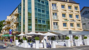 Ein Hotel mit moderner Glasfassade, Außenbereich mit Sonnenschirmen und einem sichtbaren Schild für 'Viva la moda'.