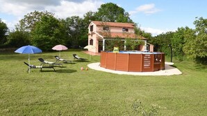 A house with a swimming pool, surrounded by a lawn with lounge chairs and umbrellas.