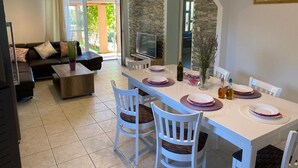 Comedor con una mesa blanca preparada para cuatro personas, sillas blancas y una pared de piedra.
