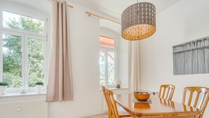 A dining area with a wooden table and chairs, a hanging light fixture, and a view of trees through the windows.
