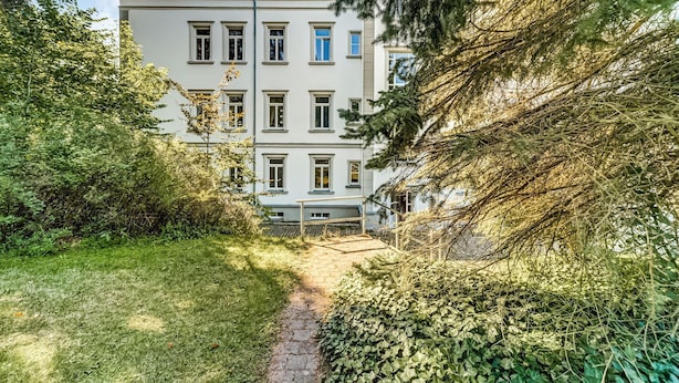A multi-story building with a central courtyard, surrounded by dense foliage and trees.