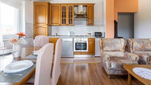 A modern kitchen with wooden cabinets, a dining area with a table set for two, and a patterned sofa. - Modern Apartment in Viskovo With Balcony (Viskovo)