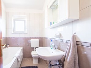 Une salle de bain équipée d’une baignoire, de toilettes, d’un lavabo et d’une serviette accrochée au mur.