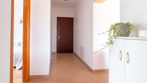 A hallway with a wooden door at the end, a white cabinet with a plant, and a bed visible through an open door. - Modern Apartment in Viskovo With Balcony (Viskovo)