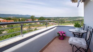 A balcony with a view of a hilly landscape, a small table with a chair, and a potted plant. - Modern Apartment in Viskovo With Balcony (Viskovo)
