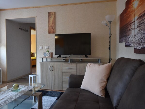 A living room with a flat-screen TV, a sofa, a coffee table, and a lamp. - Bungalow Near Salzhaff Beach Wismar (Boiensdorf)