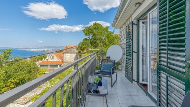 A balcony with a view of the sea, a dining table with chairs, and a green shuttered door. - Holiday Home in Podstrana Near Beach (Podstrana)