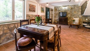 A dining area with a wooden table, chairs, and a vase of flowers. There is a stone wall and a television in the background. - Holiday Home in Podstrana Near Beach (Podstrana)
