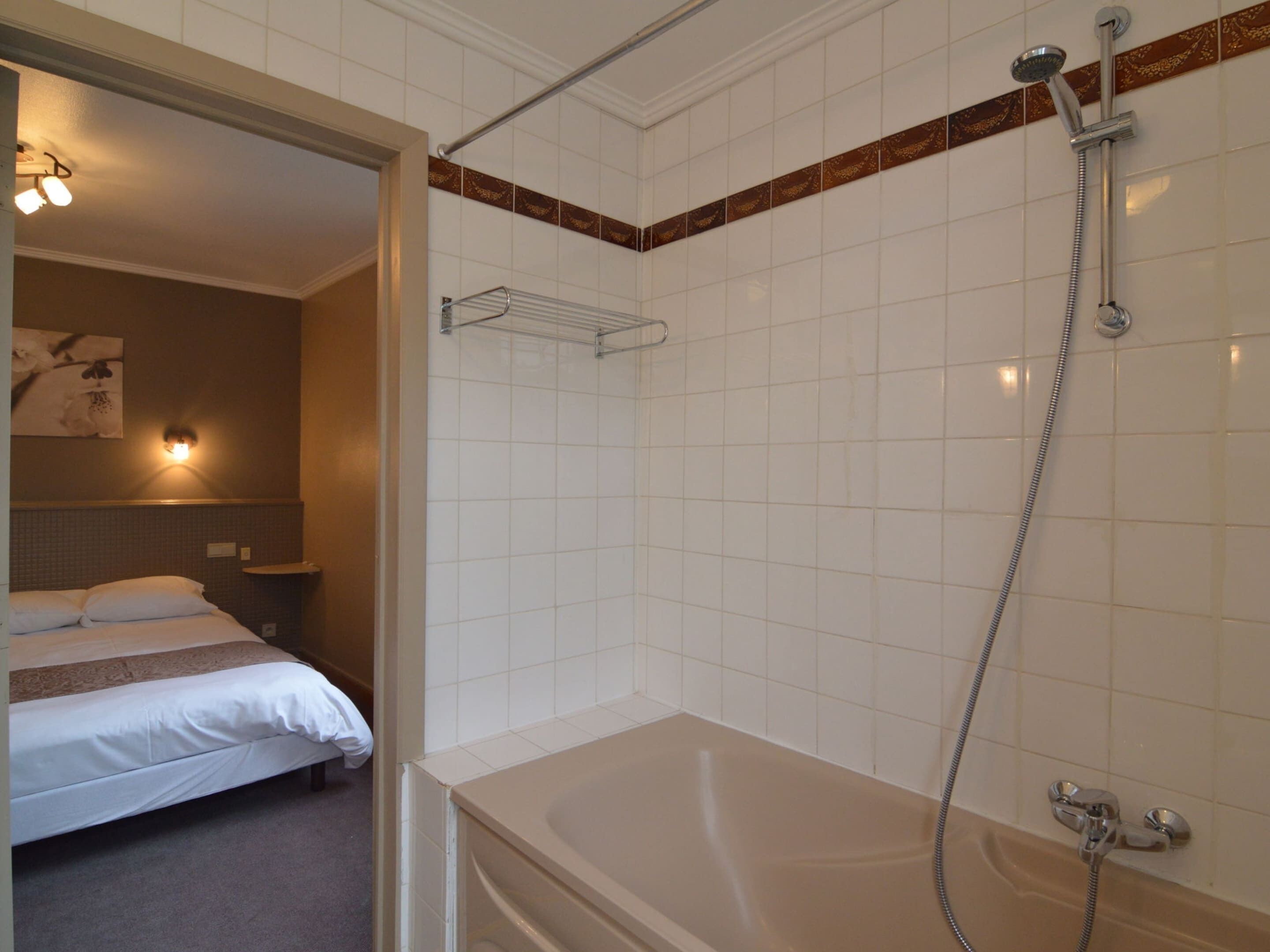 Et badeværelse med badekar, bruser og håndklædestang.