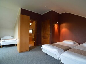Ett hotellrum med två separata sängar, en garderob i trä, ett badrum som syns genom en öppen dörr och en väggmonterad lampa.