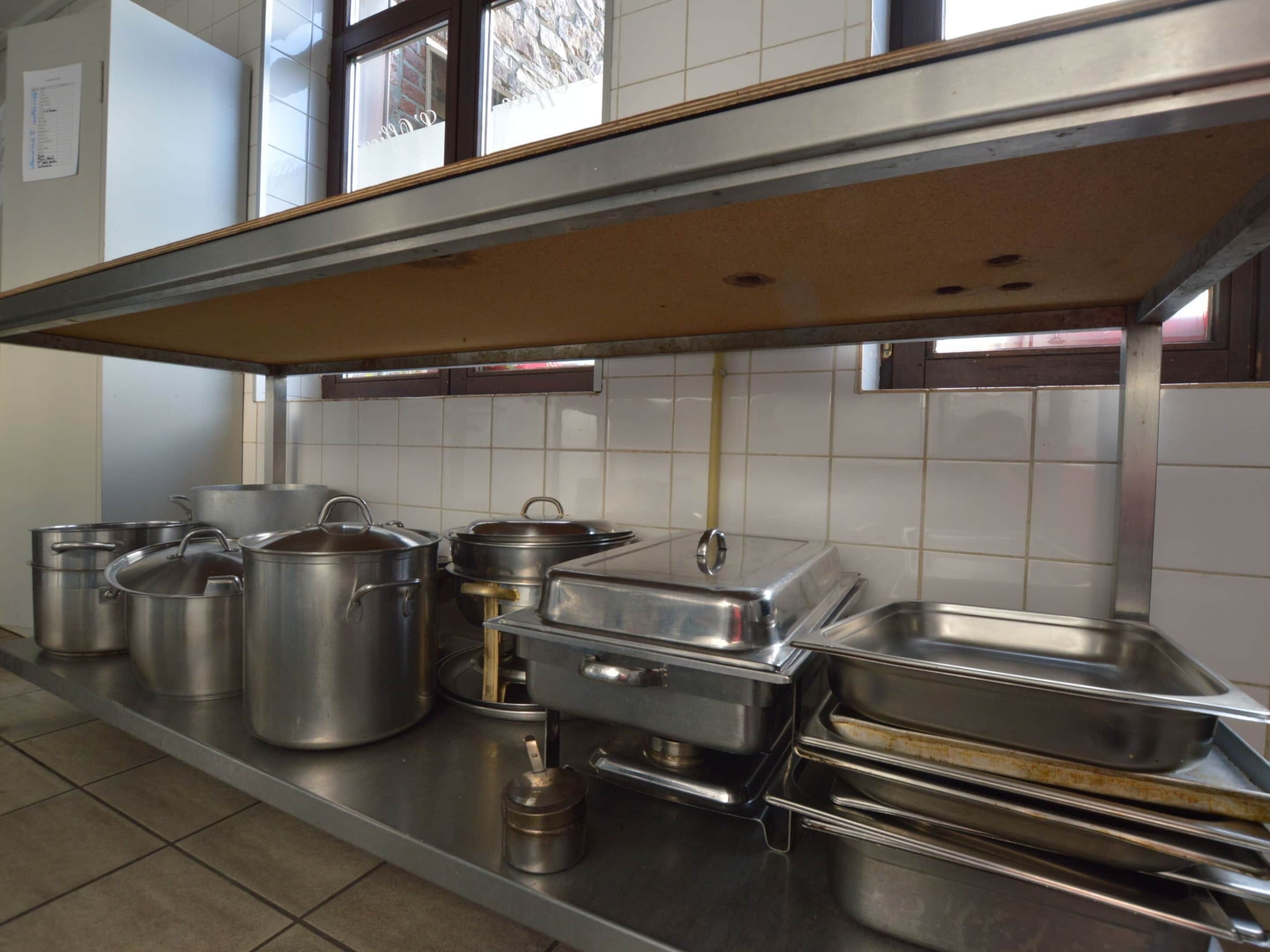 Een professionele keuken met roestvrijstalen potten, pannen en een groot industriële fornuis.