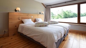 A bedroom with a wooden headboard, two beds, a large window with a view of greenery, and a wall-mounted lamp. - Holiday Home in Leglise Near Ardennes River (Léglise)
