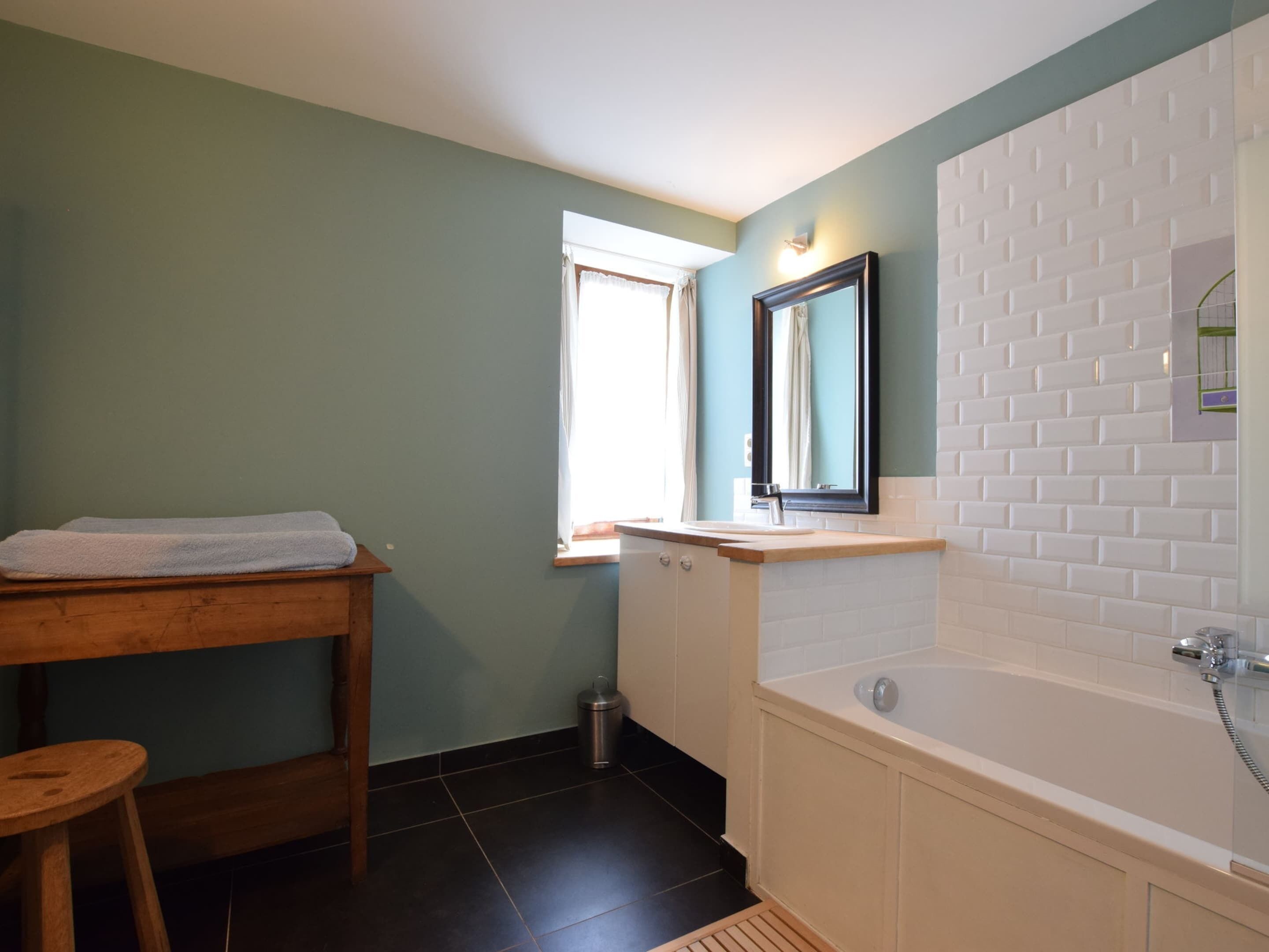 A bathroom with a wooden stool, a sink, a bathtub, and a window with curtains.