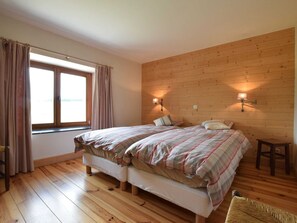 Een slaapkamer met twee bedden, houten vloeren, een raam met gordijnen en wandlampen.
