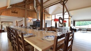 A long dining table set for a meal, wooden beams on the ceiling, a fireplace, and a view through large windows. - Holiday Home in Leglise Near Ardennes River (Léglise)