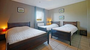Habitación de hotel con tres camas de madera, una ventana con cortinas y dos lámparas fijadas a la pared.