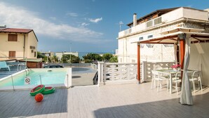 A pool area with a view of the sea, a covered seating area, and a building with a stone facade. - Apartment in Alcamo Near the Beach (Alcamo)