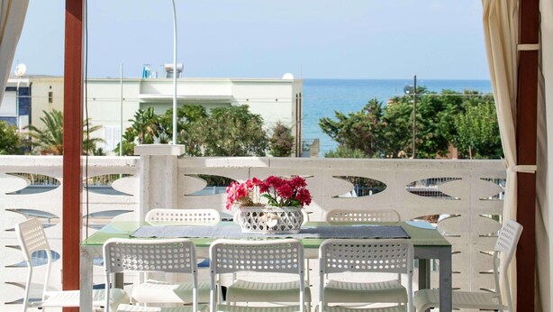 An outdoor seating area with a table and chairs, a potted plant with flowers, and a view of the sea and buildings in the background. - Apartment in Alcamo Near the Beach (Alcamo)
