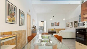A modern kitchen with a glass dining table, wooden chairs, and a built-in oven. - Apartment in Alcamo Near the Beach (Alcamo)