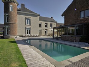 A swimming pool with a wooden deck, a brick building with a tower, and a glass-enclosed area. - Lavish Castle in Thimister With Turkish Steambath, Sauna (Thimister-Clermont)