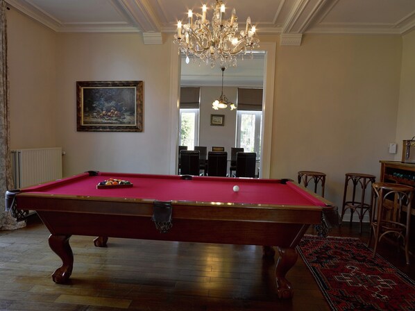 A pool table with balls, a chandelier, a framed painting, and a view to a dining area.