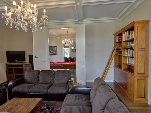 A living room with a sofa, a wooden coffee table, a television, a chandelier, and a bookshelf.
