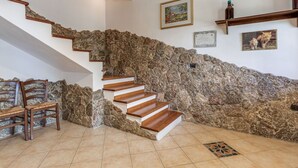 Una escalera con paredes de piedra, peldaños de madera y suelo de baldosas.