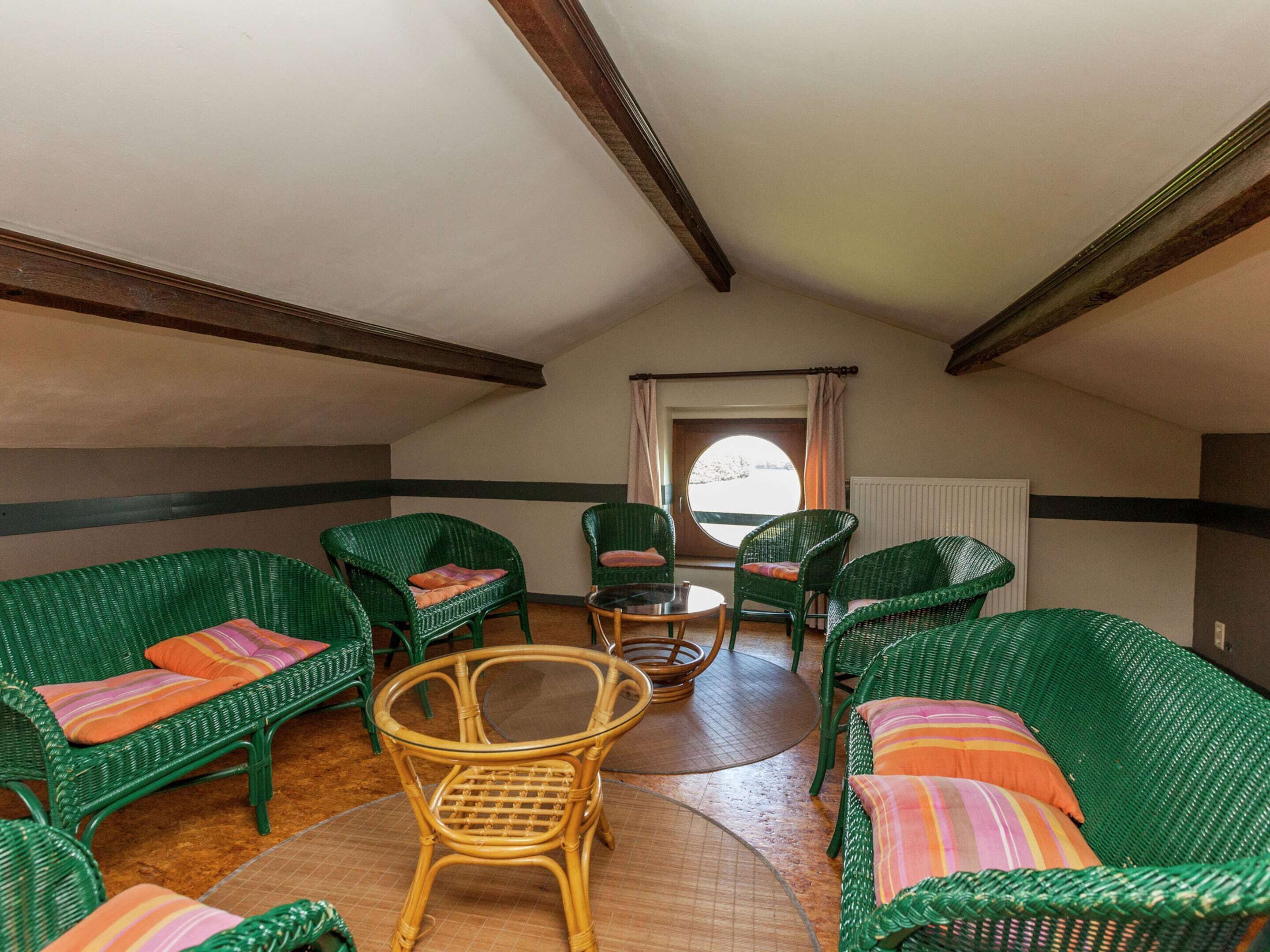 Une pièce chaleureuse, meublée de meubles en osier vert, avec une table à plateau en verre et une vue par la fenêtre.