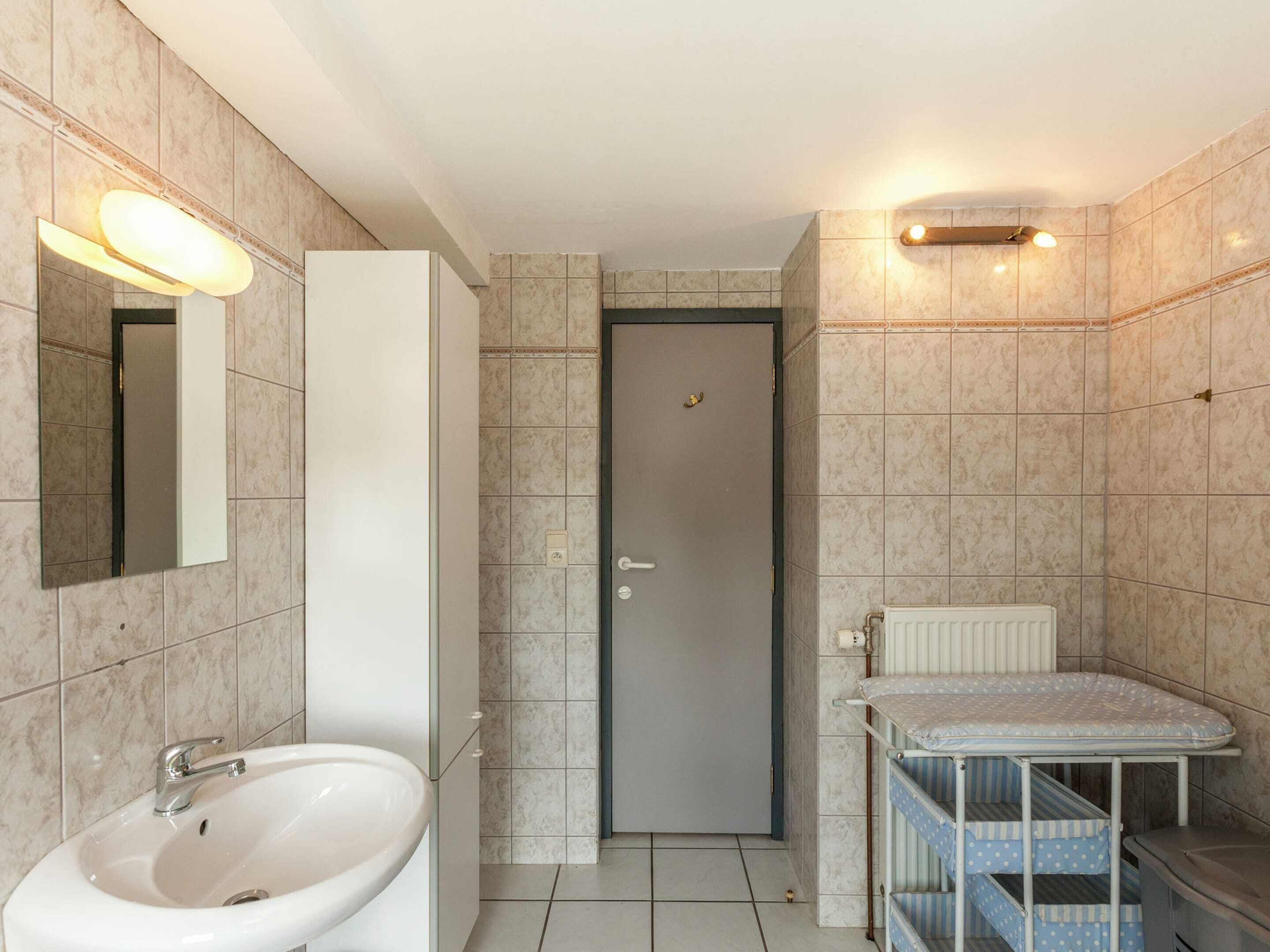 A bathroom with a sink, mirror, and a small ironing station.