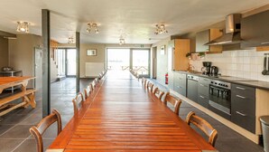 A long wooden table with chairs, a kitchen area with modern appliances, and a view of the outdoors through large windows. - Ouffet Villa With Sauna, Liege (Ouffet)
