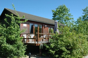 A wooden cabin with a deck, surrounded by trees.
