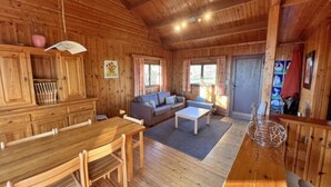 A wooden cabin interior with a dining table, sofa, and a small white table. - Holiday Home in Belgium With Kids' Playroom (Somme-Leuze)