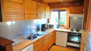 A compact kitchen with wooden cabinets, a stainless steel sink, a microwave, a stove, and a dishwasher. - Holiday Home in Belgium With Kids' Playroom (Somme-Leuze)