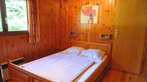 A wooden room with a bed, a window with curtains, and a door. - Holiday Home in Belgium With Kids' Playroom (Somme-Leuze)