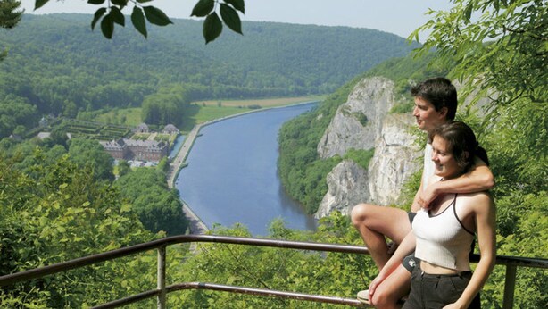 Um casal sentado em um corrimão com vista para um rio e uma paisagem verdejante.