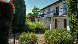 A two-story building with a balcony, surrounded by greenery and a paved pathway. - House in Noiseux With Bubble Bath & Garden (Somme-Leuze)