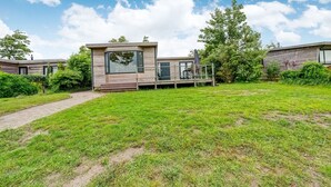 A modern house with a large glass window, a deck, and a grassy yard. - Elegant Chalet in Anjum near Lauwersmeer Lake (Anjum)