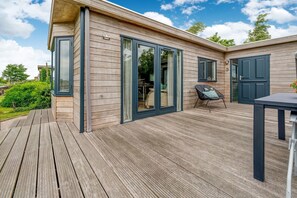 Una casa moderna de madera con terraza, puertas correderas de vidrio y un pequeño espacio de esparcimiento al aire libre.