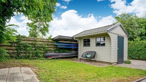 A small shed with a window and a door, a kayak, and a chair in a backyard with a paved area and a wooden fence. - Elegant Chalet in Anjum near Lauwersmeer Lake (Anjum)