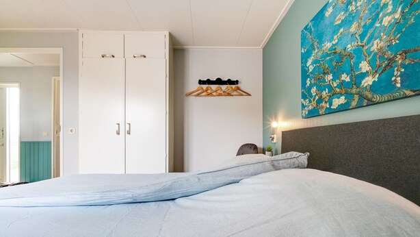 A bedroom with a bed, a wardrobe, a painting, and a wall-mounted coat rack. - Elegant Chalet in Anjum near Lauwersmeer Lake (Anjum)