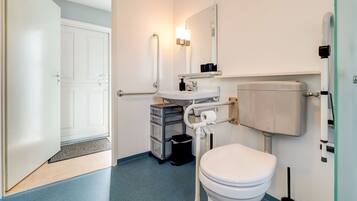 A modern bathroom with a white toilet, a sink, and a mirror. There is a door leading to another room and a trash bin next to the sink.