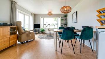 A modern living room with a sofa, a dining table with chairs, a TV, and a bookshelf.