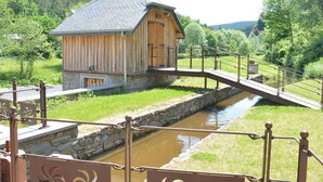 Un bâtiment en bois avec des fondations en pierre, un pont métallique et un canal d’eau.