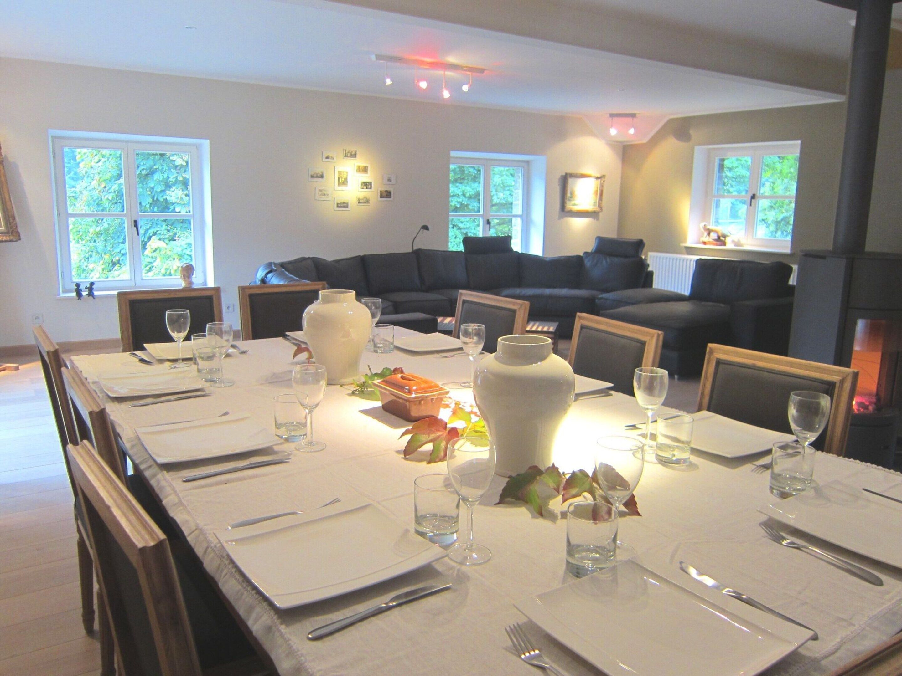 A dining area with a long table set for a meal, surrounded by a black sofa and a fireplace.