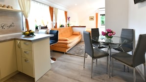 Un salon moderne comprenant un canapé, une table à manger avec des chaises, un coin cuisine avec un comptoir et des placards, et un téléviseur fixé au mur.