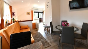 Un salon moderne comprenant un canapé, une table à manger avec des chaises, un téléviseur à écran plat fixé au mur et un escalier menant à l’étage supérieur.