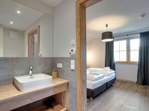 A modern hotel room with a large mirror, a wooden vanity, a bed with two pillows, a bedside table, and a window with curtains. - Chalet in Hollersbach / Salzburg Near ski Area (Hollersbach im Pinzgau)