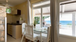 A kitchen with a stone wall, a microwave, and a sink. There is a glass table with two chairs and a potted plant. A large window offers a view of the sea. - Captivating Holiday Home in Tribanj near Sea (Starigrad)