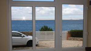 A view through a door with a white car parked outside, a white fence, and a beach with the sea in the background. - Captivating Holiday Home in Tribanj near Sea (Starigrad)