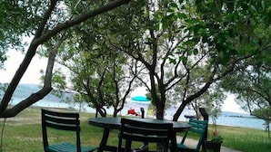 An outdoor seating area with tables and chairs under trees, overlooking a body of water. - Your Perfect Adriatic Getaway (Starigrad)
